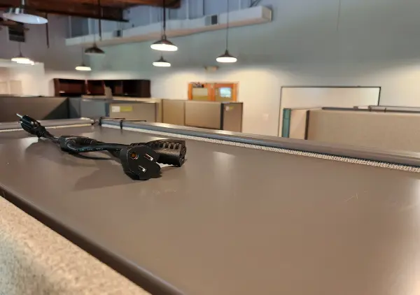 A close-up view of an electric cable resting on a cubicle partition in an office space, with blurred cubicles in the background